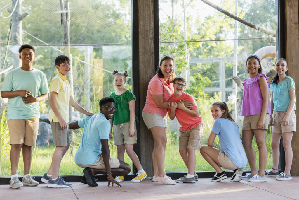 A group of children smiling at the camera while enjoying a field trip at the zoo.